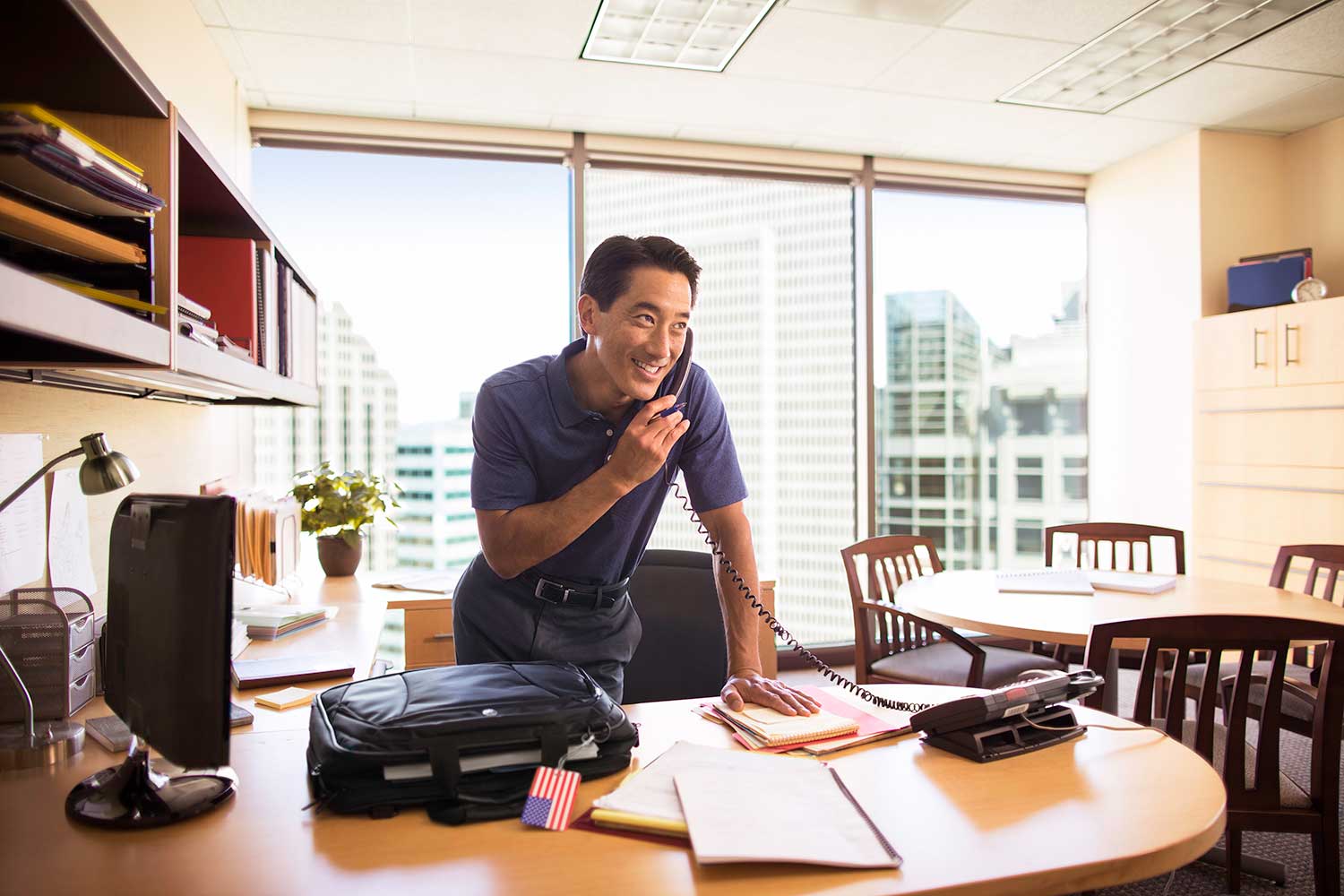 Man smiles while talking on the phone in his office