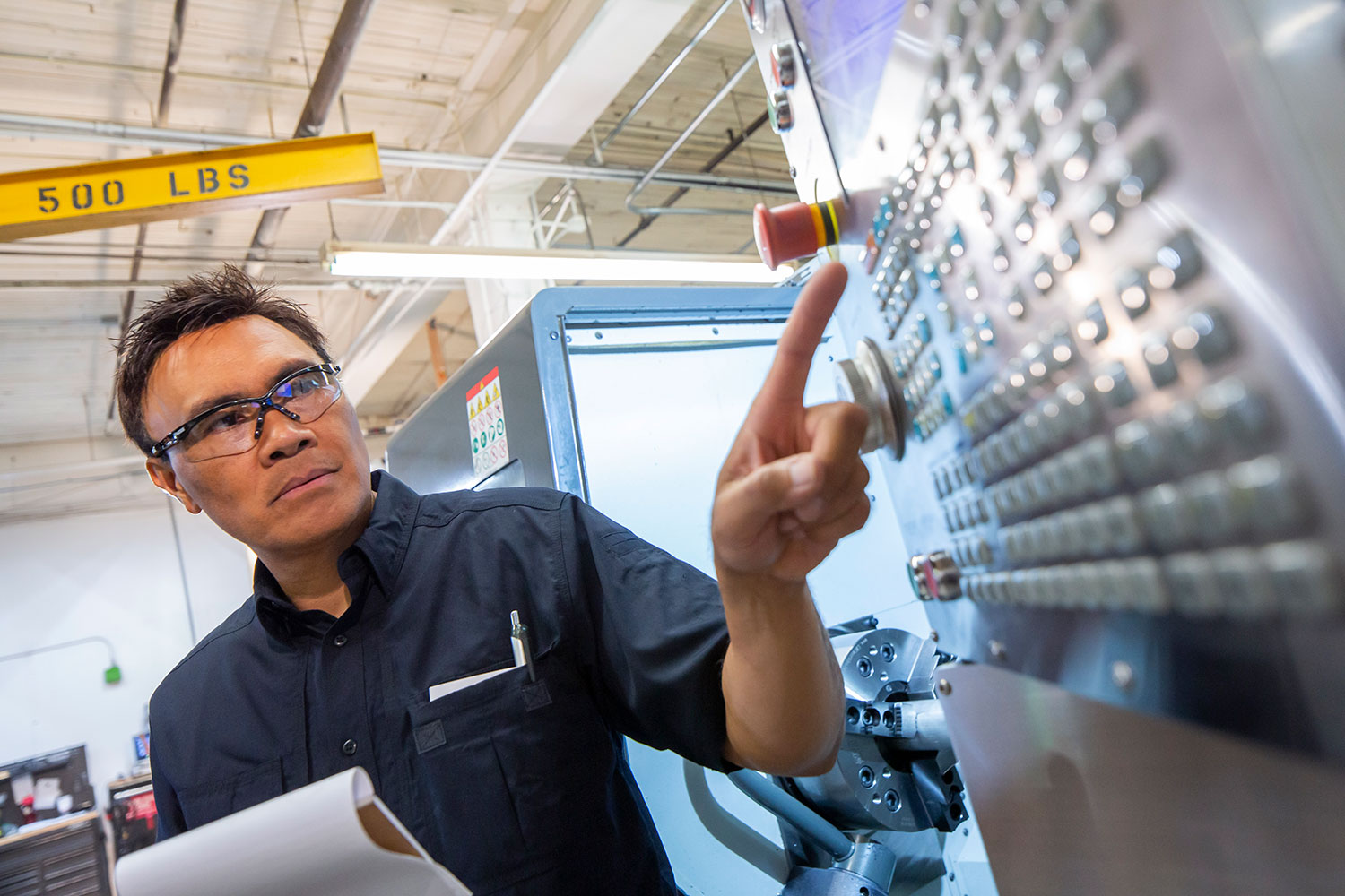 Man wearing safety glasses presses buttons on a machine