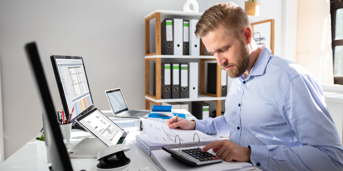 Man typing on a calculator with papers surrounding him