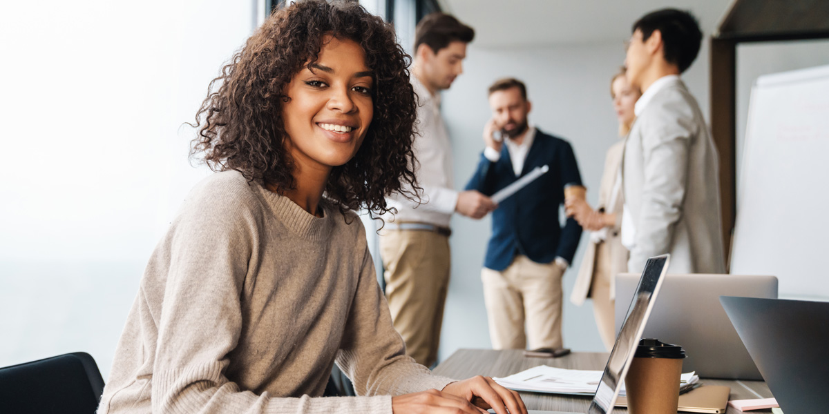 Women smiling while on computer with a group of young professionals behind her